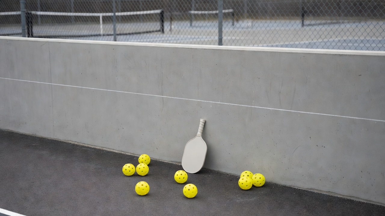 Outdoor pickleball wall drill setup with paddle leaning on concrete wall and yellow balls
